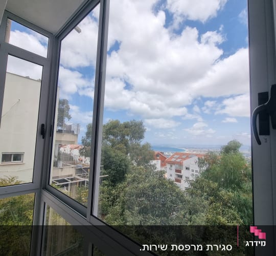 חלון אלומיניום עם נוף לעצים ושמים מעוננים